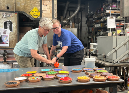 Emily Drabinski and glass artist Elodie Holmes working together to fashion a piece of hot glass in Holmes' studio.