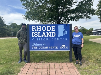 Nikita Carpenter Jr. and ALA President Emily Drabinski pose near a sign at the Rhode Island Visitor Center. 