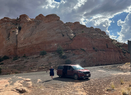 Emily Drabinski stands next to the rental van used on the cross-country tour. Behind her the spectacular landscape of the Southwest.