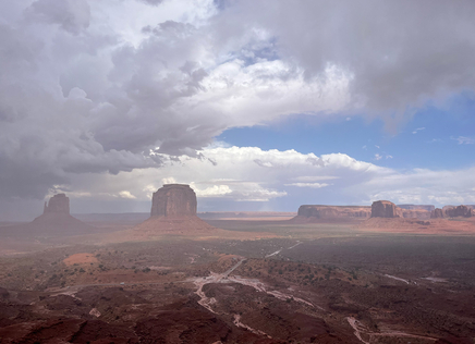 A panoramic view of Monument Valley with buttes in the distance and storm clouds gathering. 