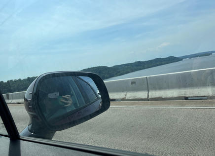 Photo taken from a car window as it crosses a bridge. In the car's side mirror is a reflection of the person holding the camera, ALA President Emily Drabinski. 