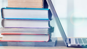 Various books stacked up against an open laptop