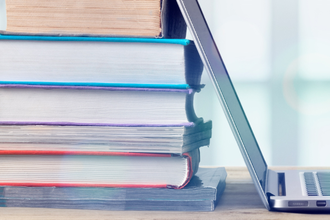 Various books stacked up against an open laptop