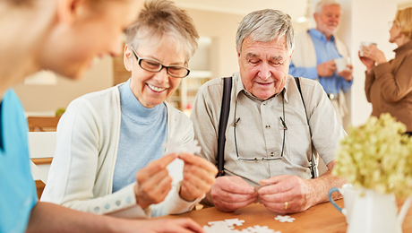 Female and male seniors fitting together blank puzzle pieces with guidance from a female medical professional.