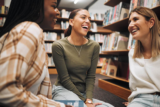 Three women meeting in the library and laughing stock image