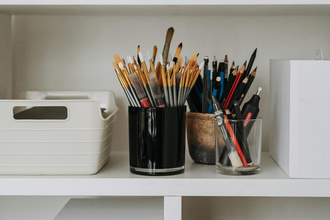 White shelves with office supplies, paint brushes, and pens on it