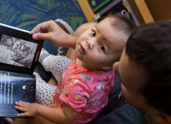 a papa reads with his baby in the library